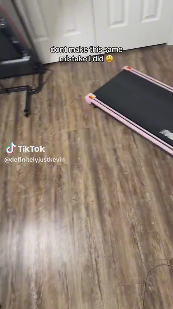 The walking pad next to a desk with the handrail up