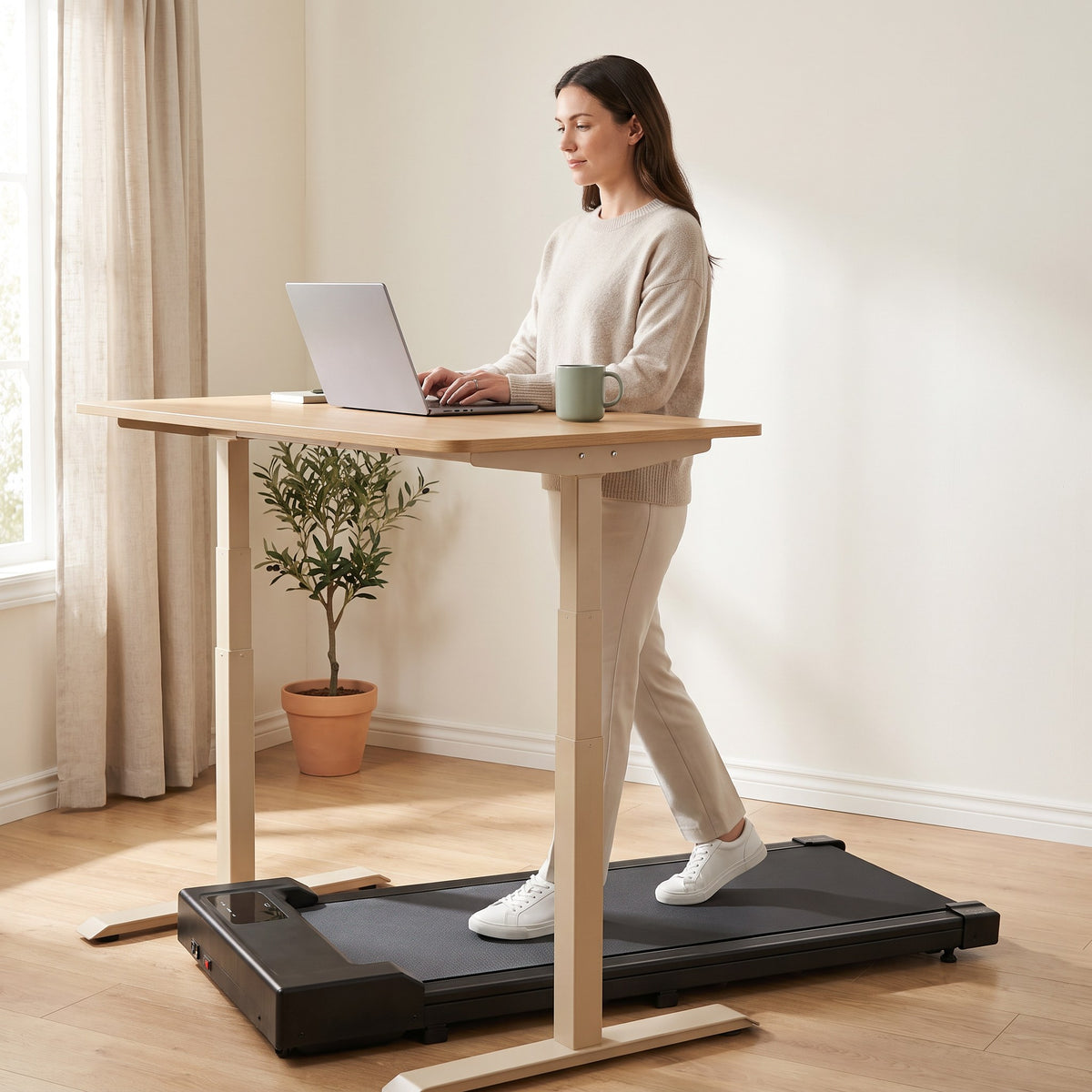 Woman walking on the Saunterly Walking Pad while typing on a laptop at a standing desk in a bright home office